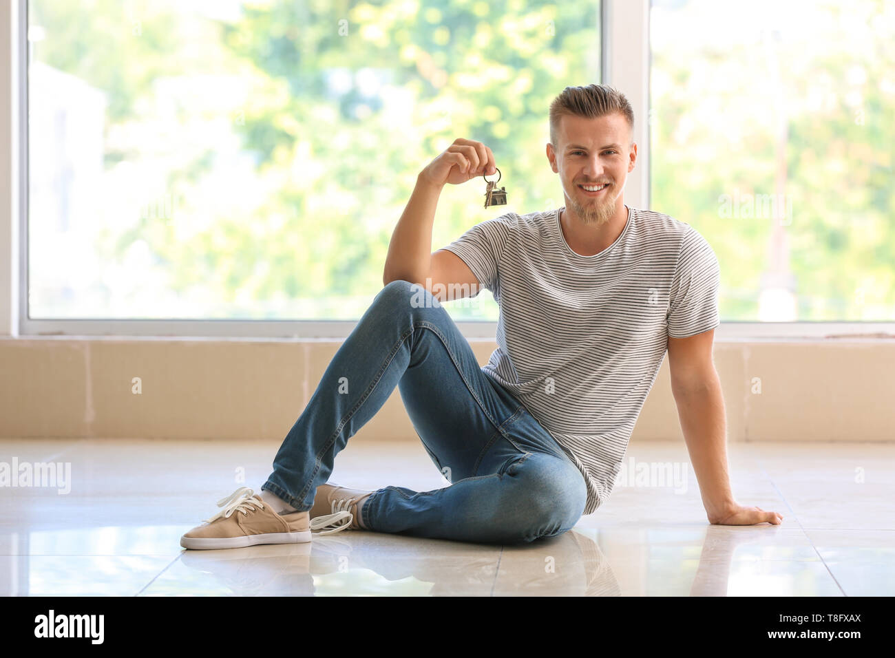 Happy young man with key from his new house indoors Stock Photo
