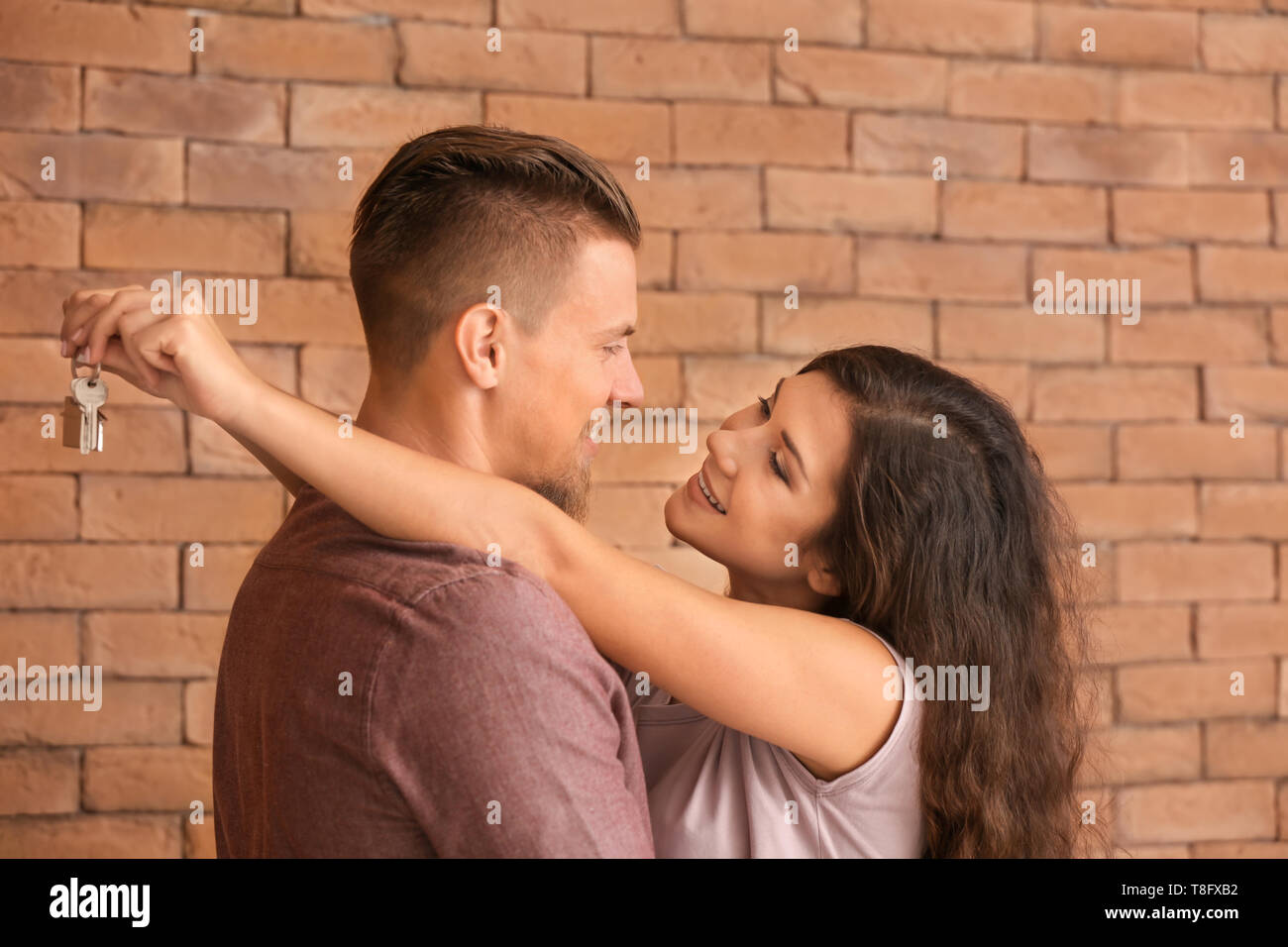 Happy young couple with key from their new house near brick wall Stock ...