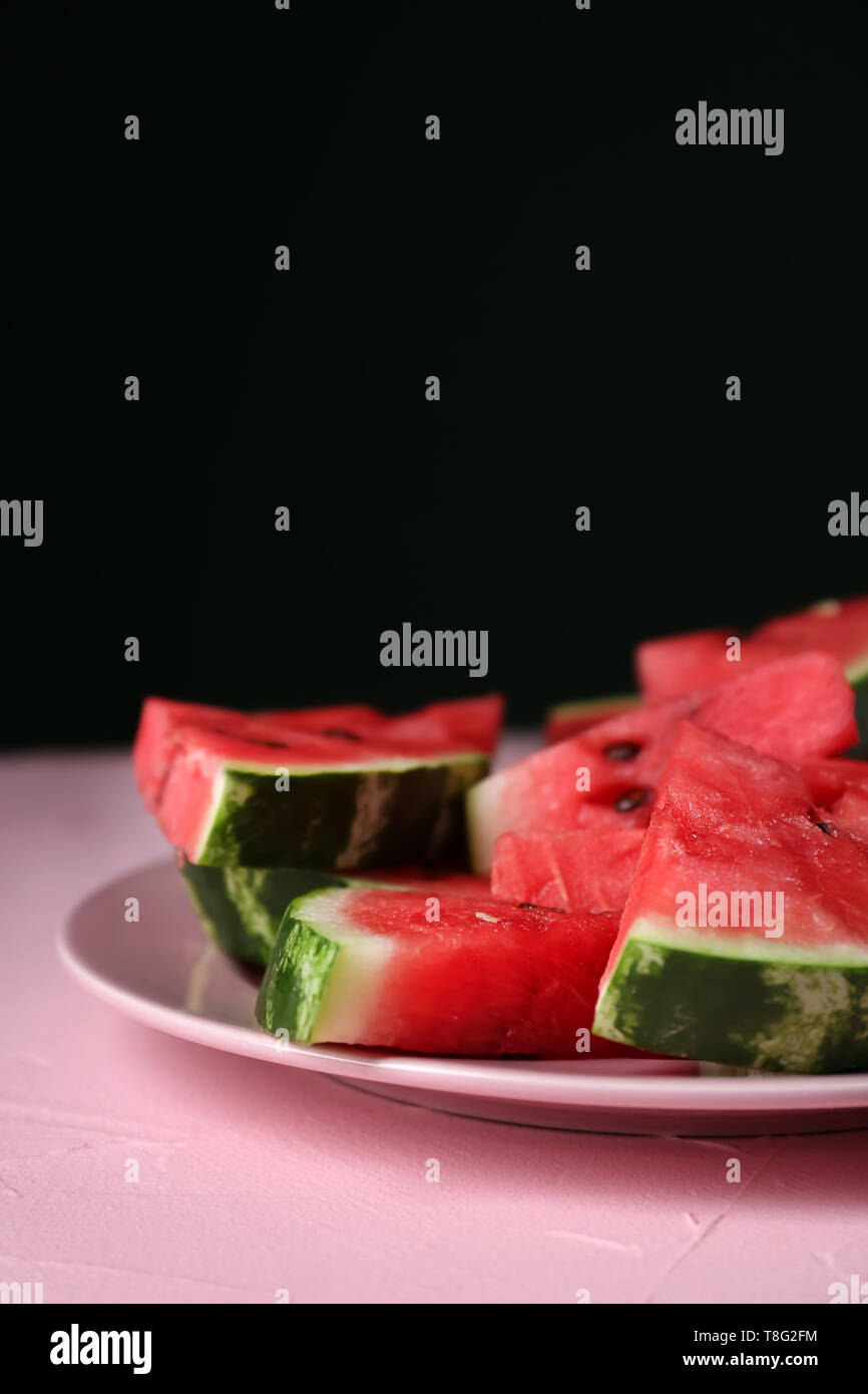 Plate with slices of ripe watermelon on color table against dark