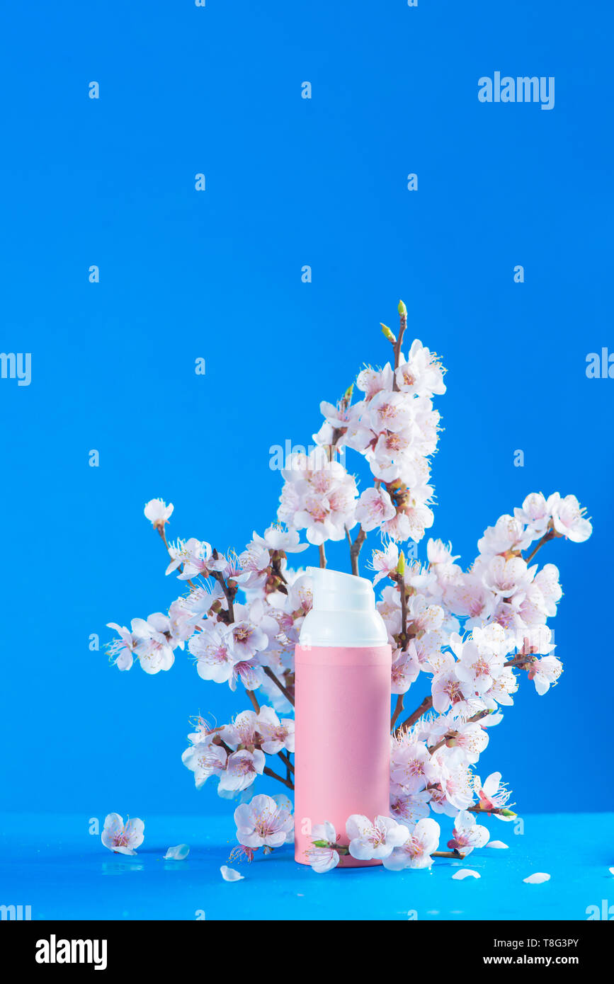 Cherry blossom cosmetics concept. Pink creme tube with spring flowers on a sky blue background with copy space. Stock Photo