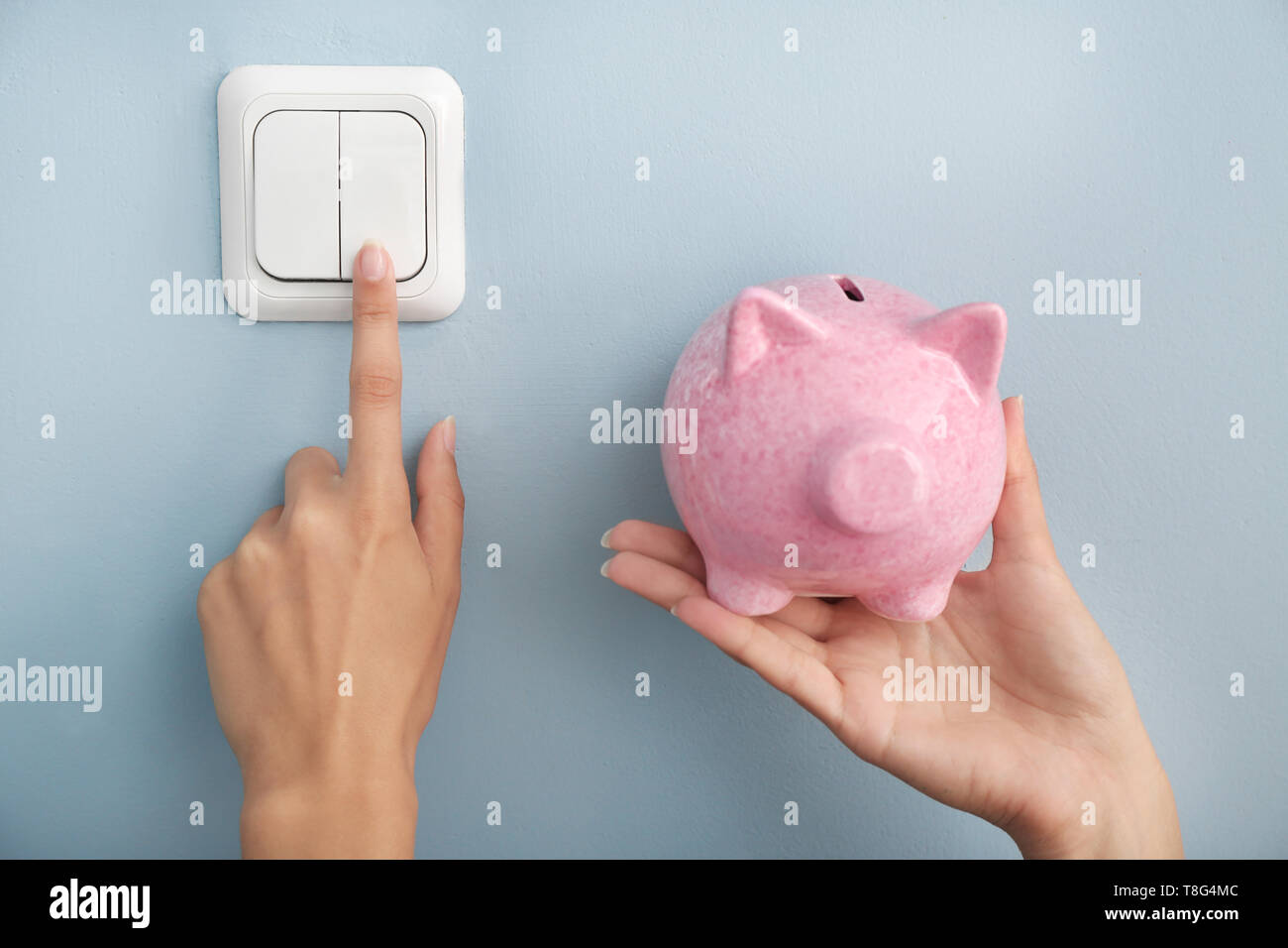 Woman with piggy bank switching off the light. Electricity saving concept Stock Photo