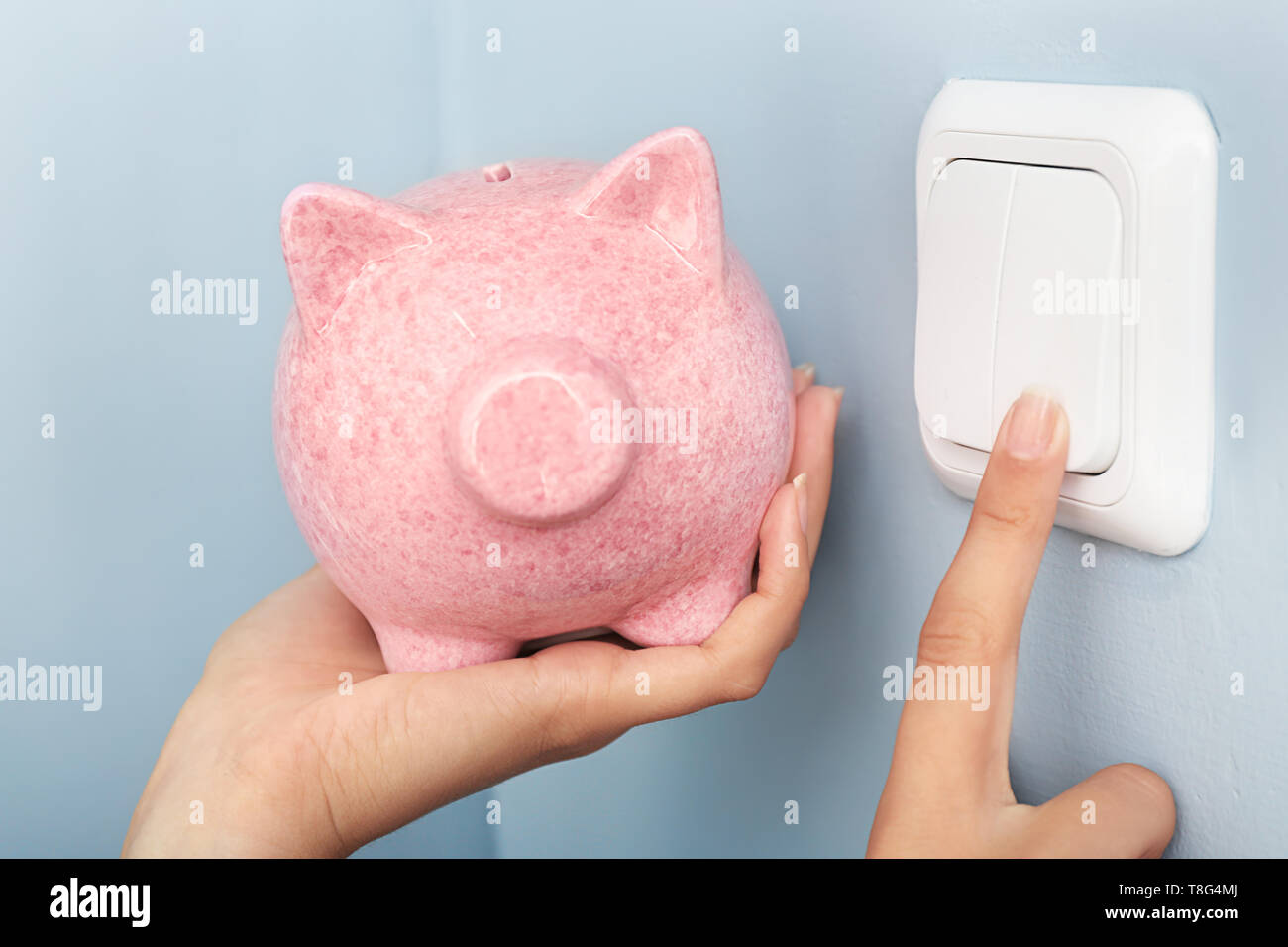 Woman with piggy bank switching off the light. Electricity saving concept Stock Photo