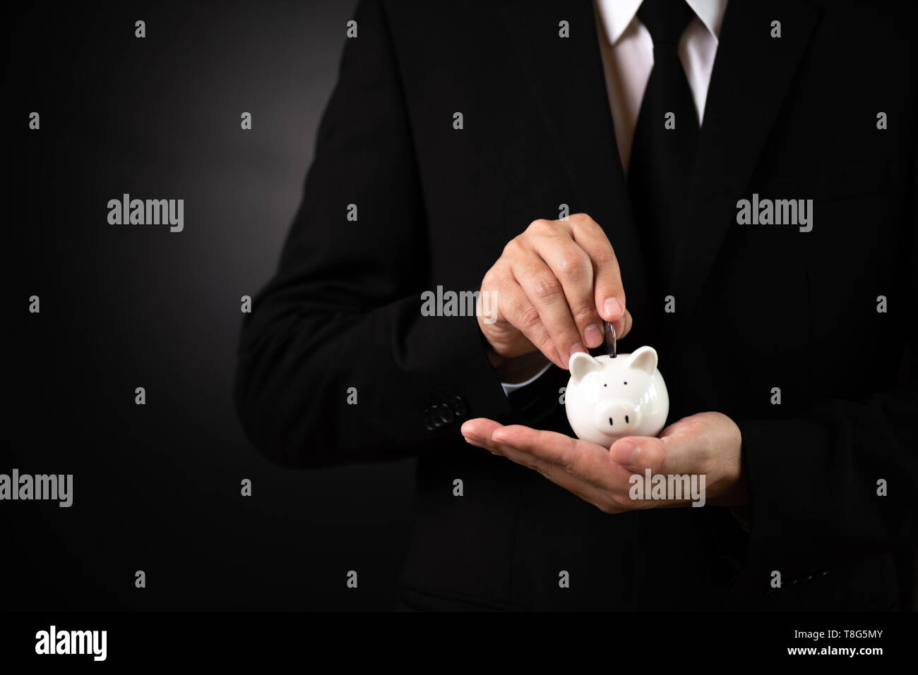 Businessman in suit is hand putting coin into piggy bank and . Finance ...