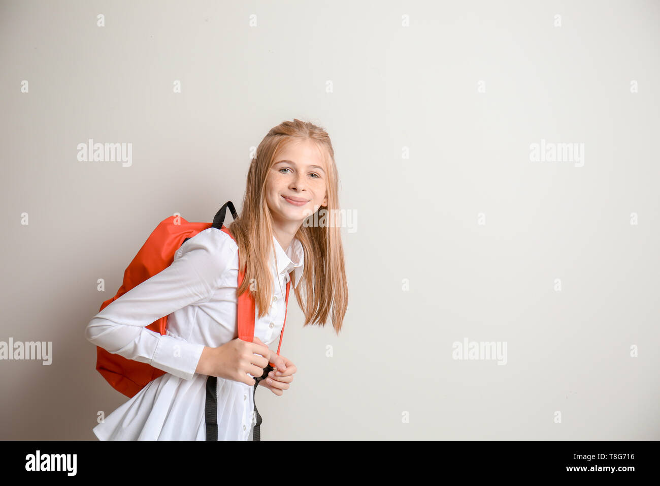 Cute schoolgirl with backpack on light background Stock Photo - Alamy