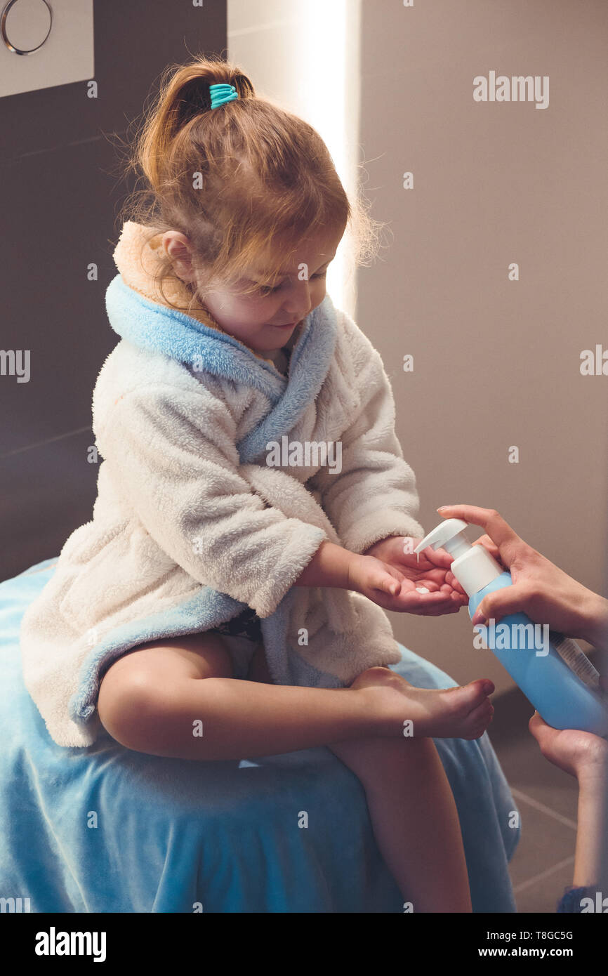 Mother applying moisturizing cream on her daughter's legs after bath