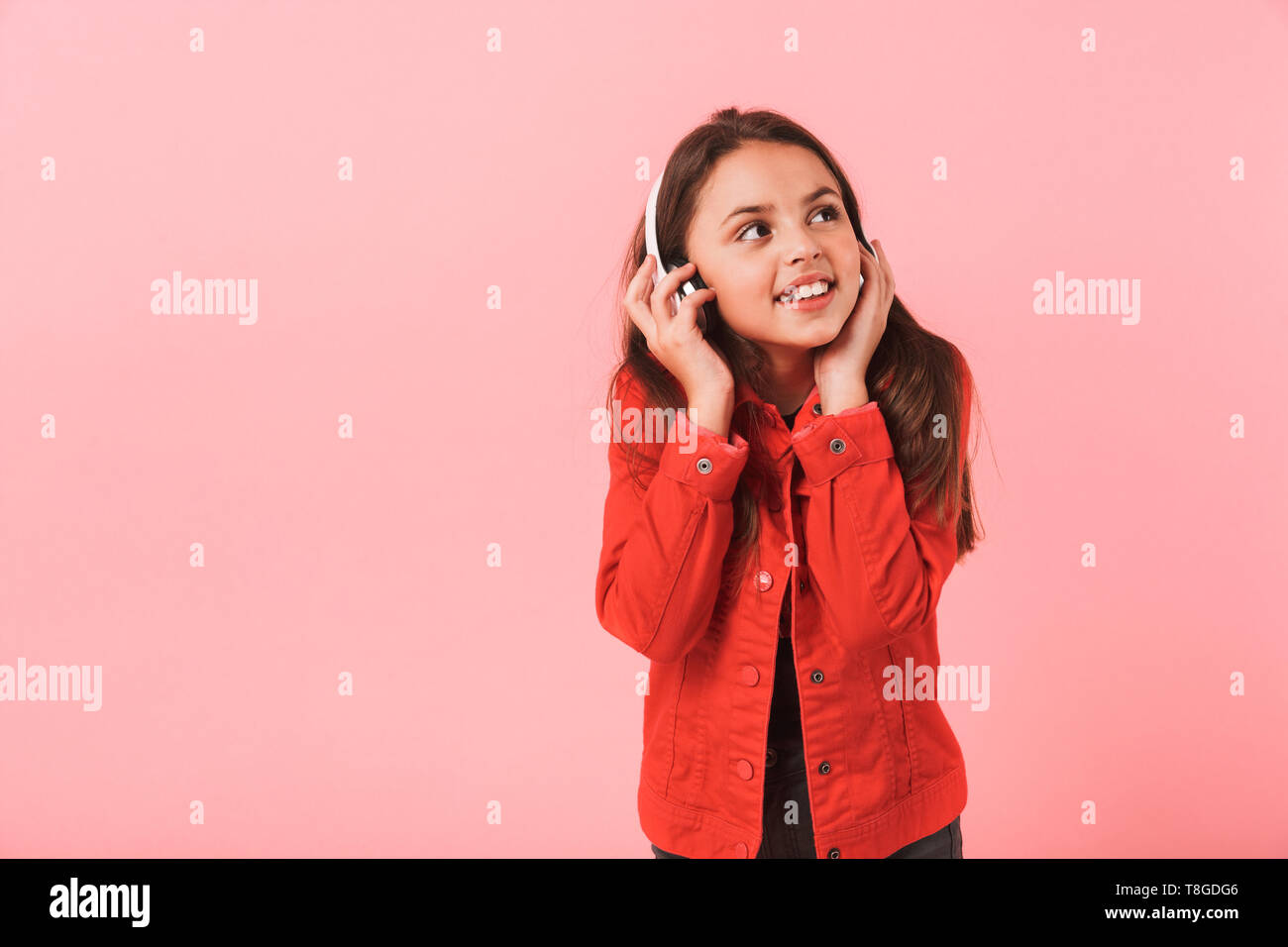Image of pretty little girl in casual wearing headphones listening to music isolated over red background Stock Photo