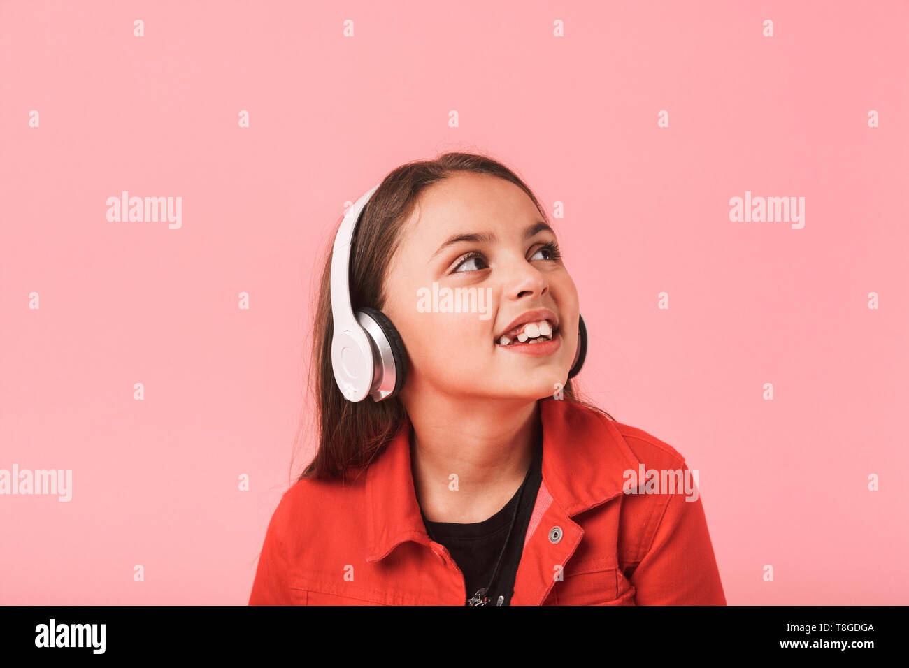 Image of european little girl in casual wearing headphones listening to music isolated over red background Stock Photo