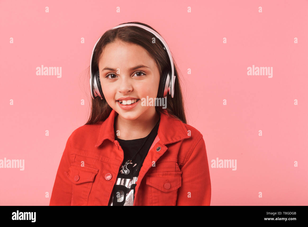 Image of joyous little girl in casual wearing headphones listening to music isolated over red background Stock Photo
