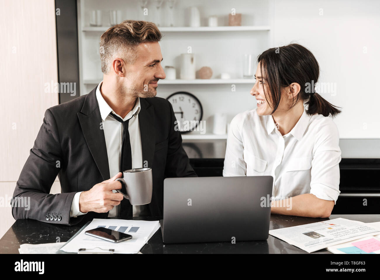 Two colleagues working on a project together while sitting at the office desk, using laptop, analyzing documents Stock Photo