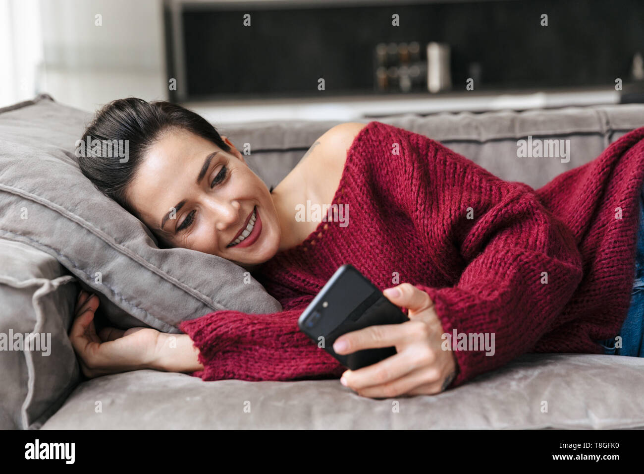 Image of a beautiful woman indoors in home on sofa using mobile phone. Stock Photo