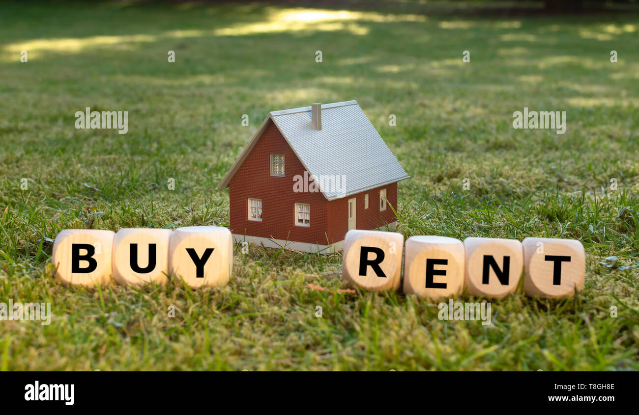 Concept for buying or renting a house. A miniature house placed on green meadow. Dice form the words "BUY" and "RENT". Stock Photo