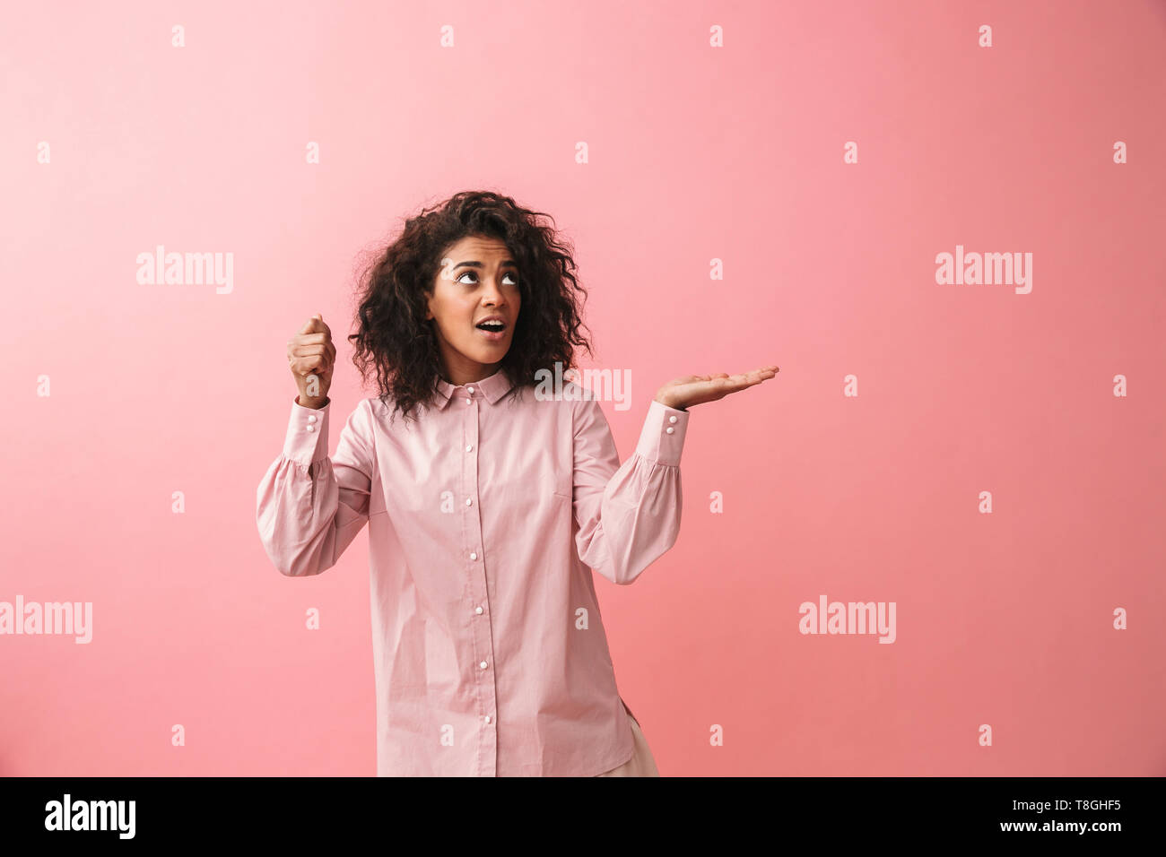 Image of a happy beautiful young african woman posing isolated over pink wall background showing copyspace imagine that she holding umbrella. Stock Photo