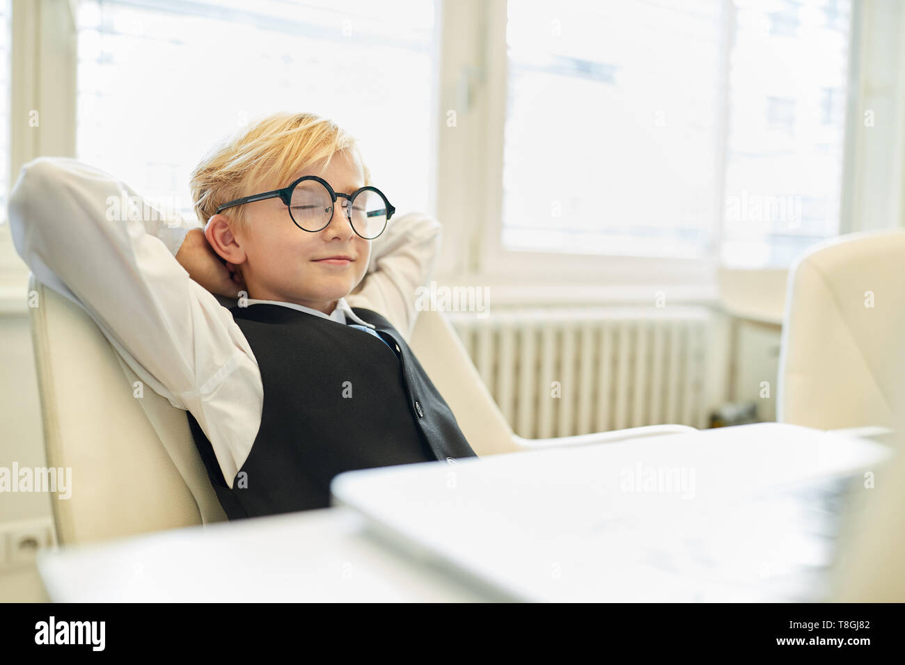 Relaxed child sits as a boss in the office with eyes closed while dreaming Stock Photo