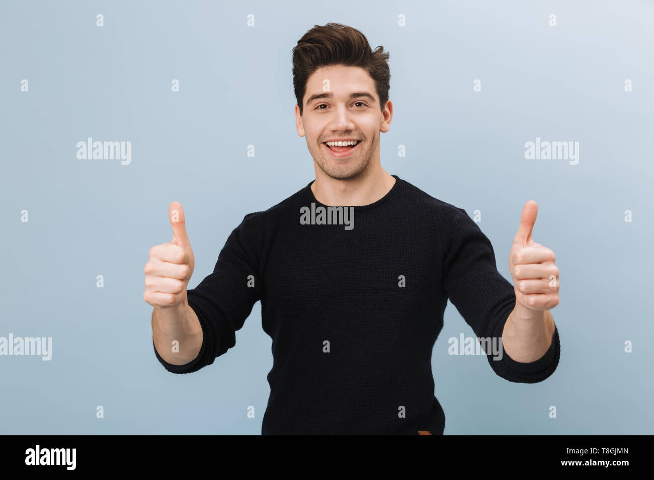 Portrait of a cheerful handsome young man standing isolated over blue background, giving thumbs up Stock Photo