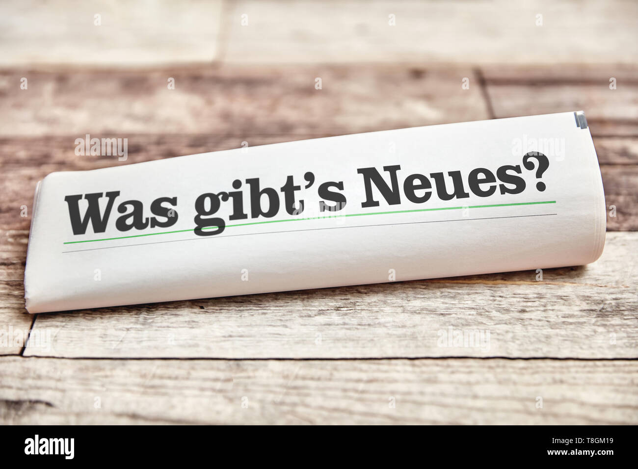 German slogan 'Was gibt's Neues?' (What's new?) is on front page of a folded newspaper on a wooden table Stock Photo