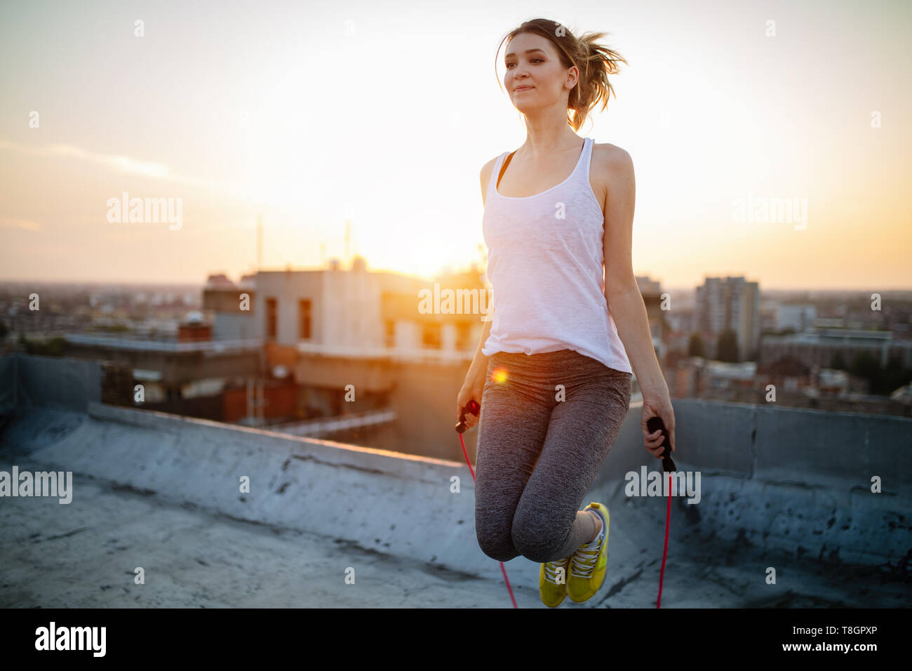 Portrait of fit young woman with jump rope on rooftop. Fitness female doing skipping workout outdoors on a sunny day. Stock Photo