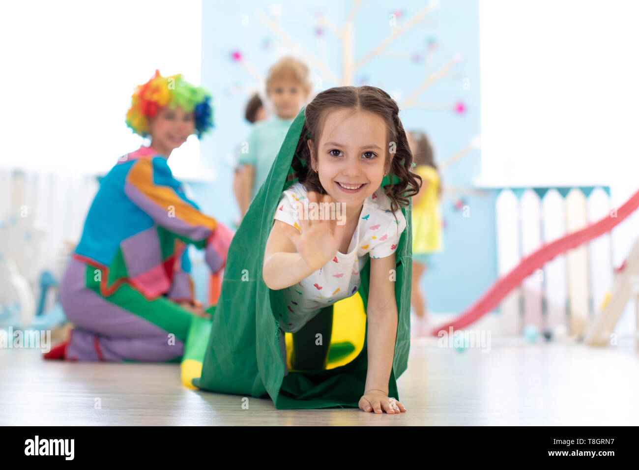 Children kids playing with clown on birthday party in entertainment centre. Child girl climbing through tunnel Stock Photo
