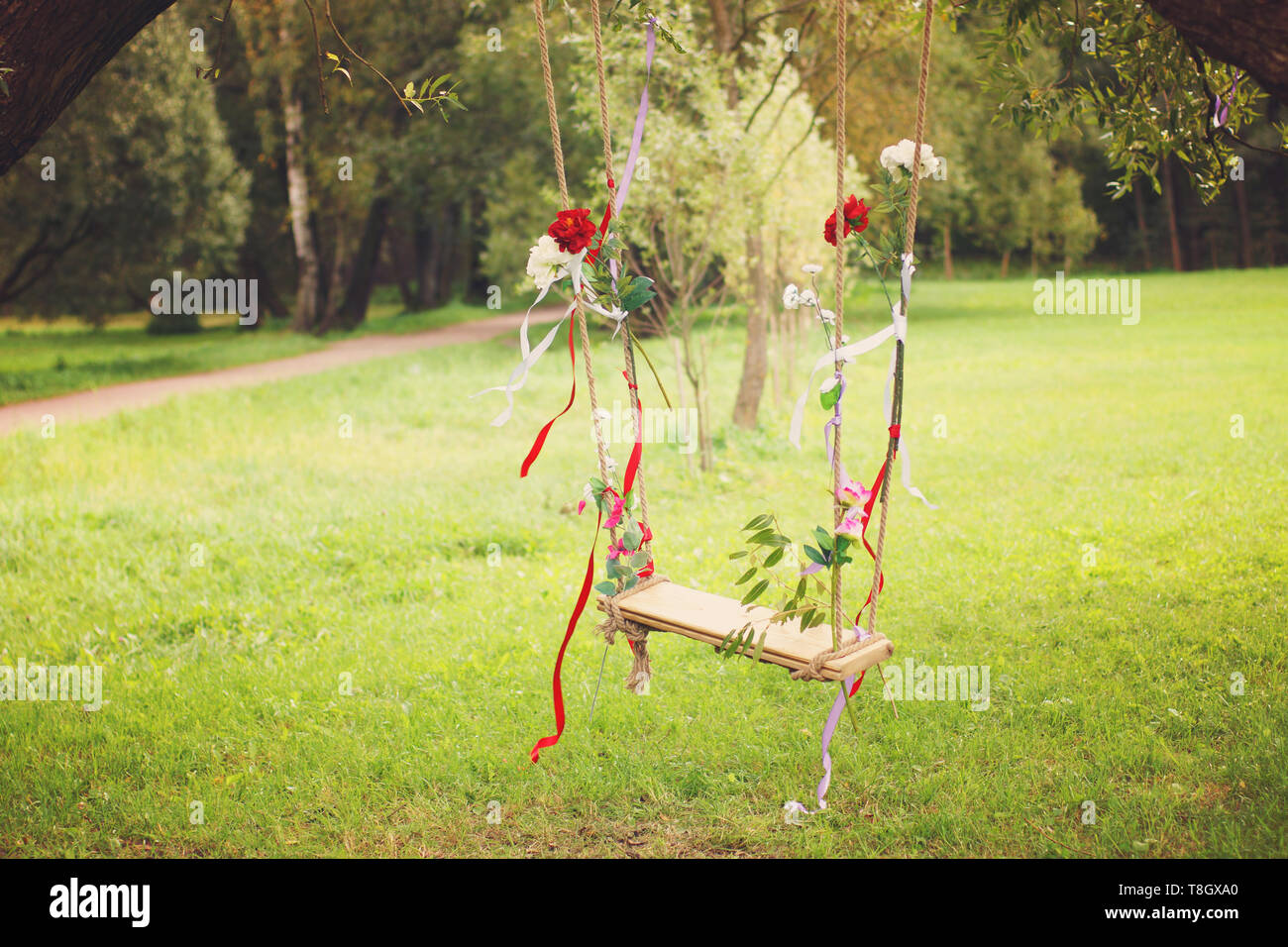 Swings decorated with ribbons and flowers hanging on a tree in a summer park Stock Photo