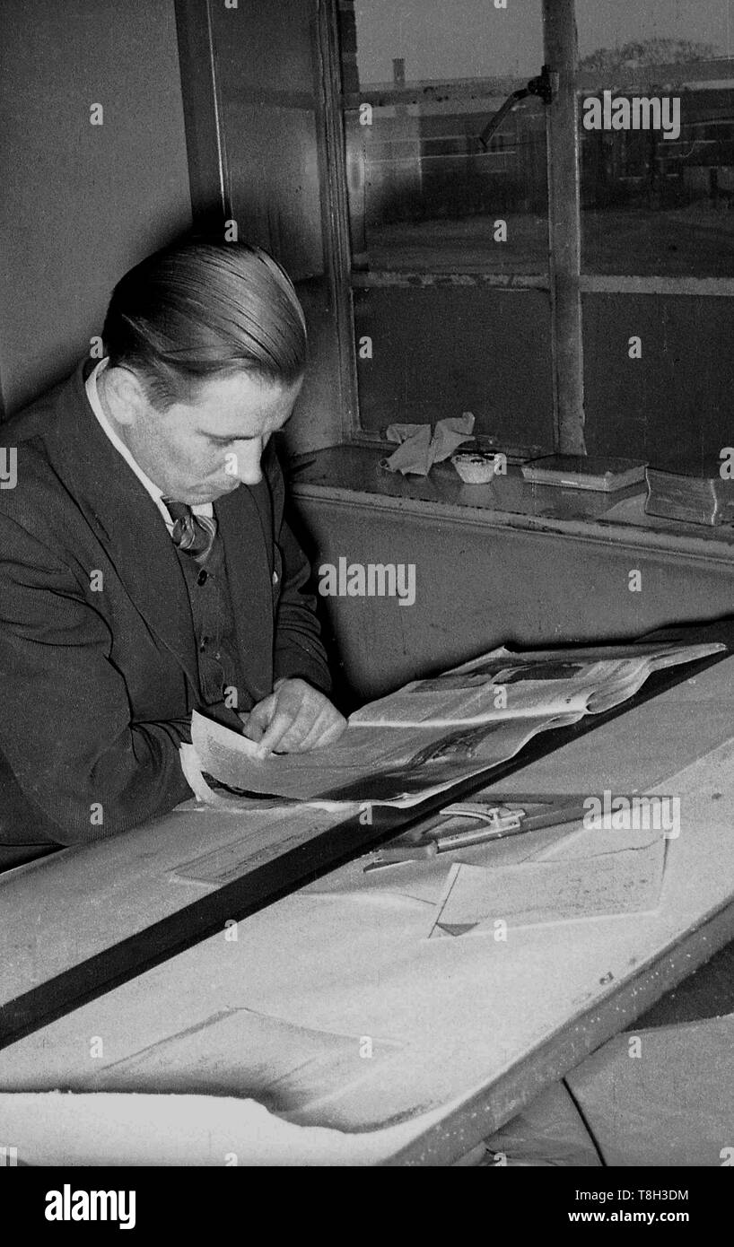 1950s, historical, suited male architect or draughtsman has a break from work, reading a newspaper or magazine at his drawing office by the window. Stock Photo