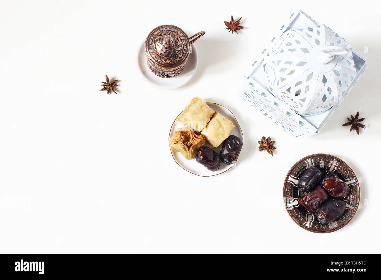 Ramadan Kareem greeting card, invitation. White lantern, bronze plate with dates fruit, baklava pastry, coffee cup on table. Iftar dinner. Eid ul Adha Stock Photo
