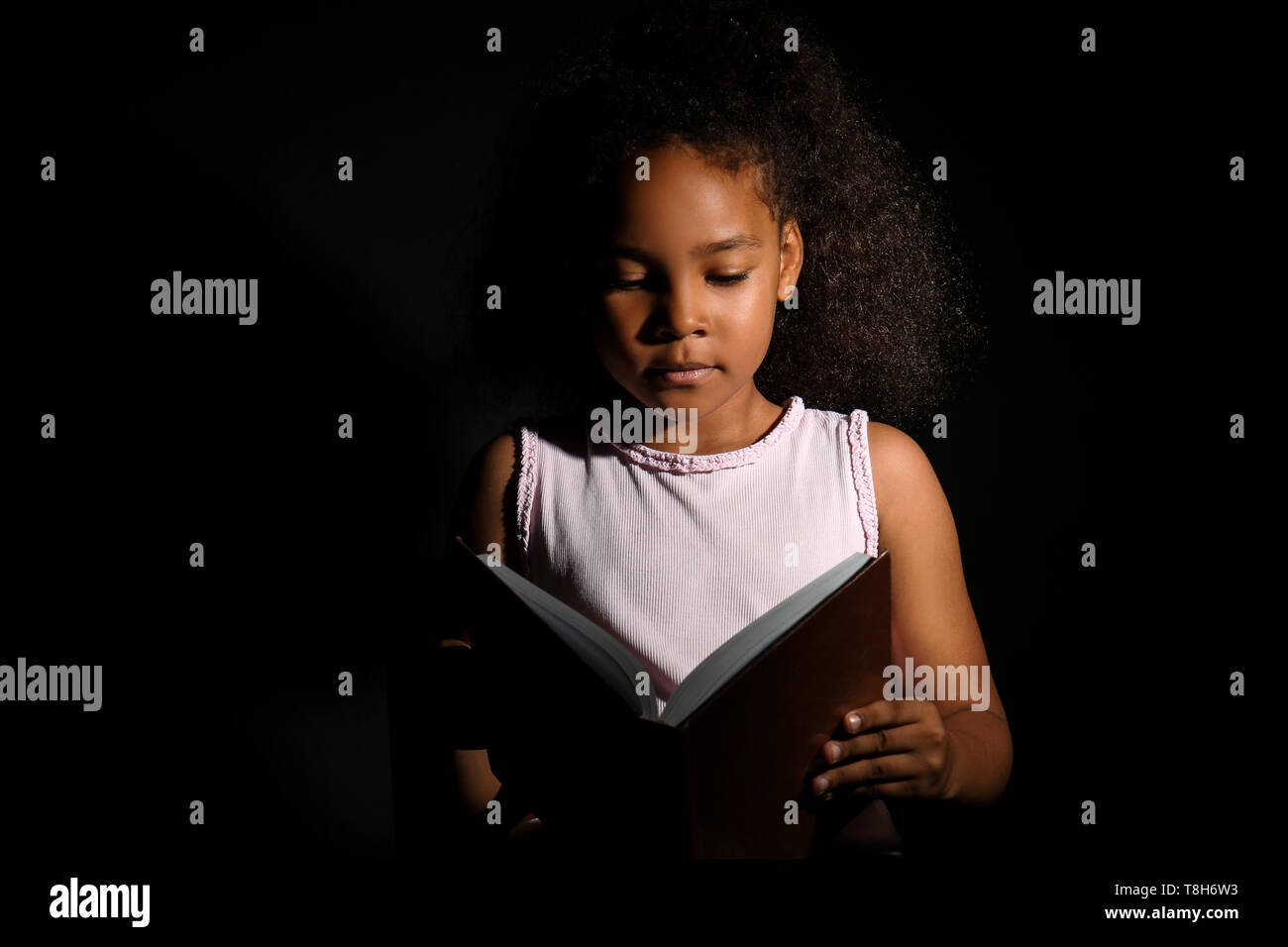 Little African-American girl reading book on dark background Stock ...