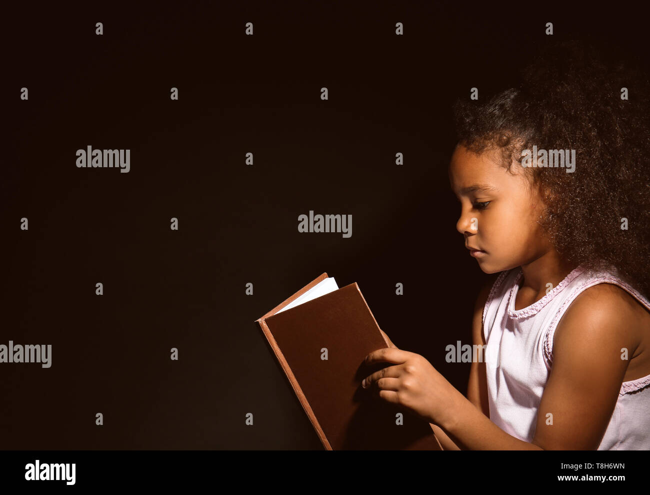 Little African-American girl reading book on dark background Stock ...