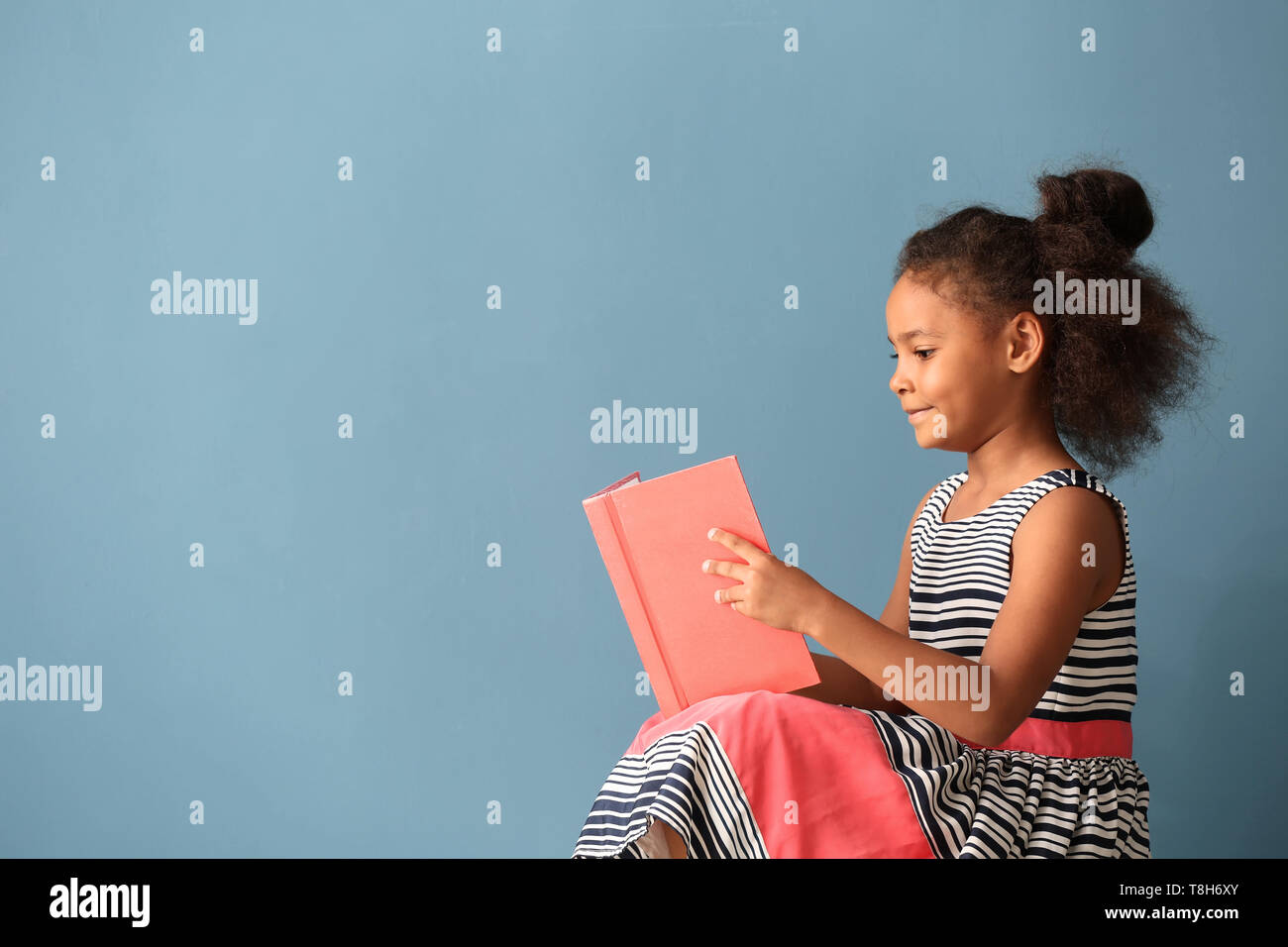 Little African-American girl reading book on color background Stock ...