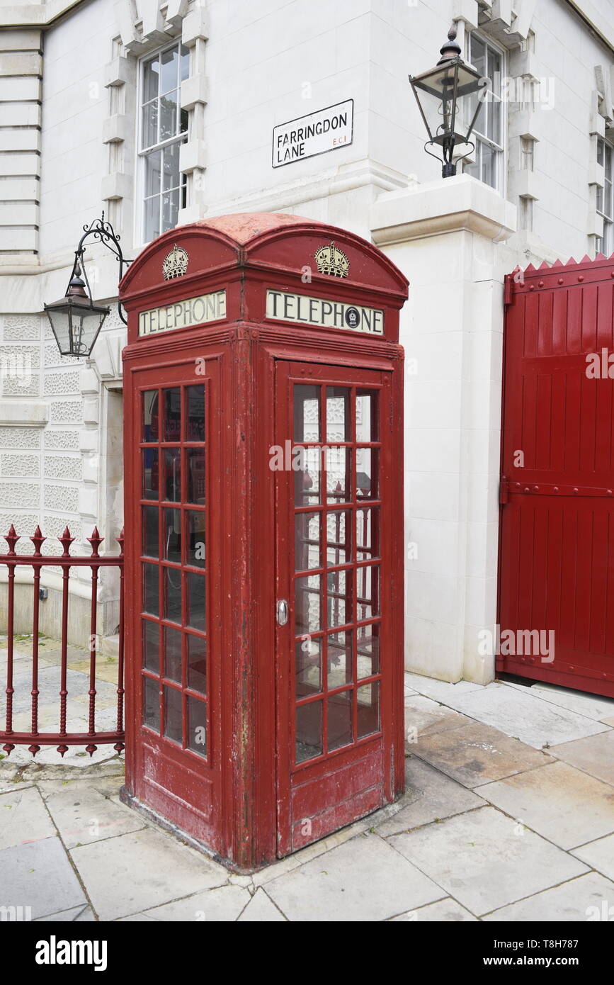 Traditional red London telephone box, next to a red gate. Farringdon Lane, London Stock Photo