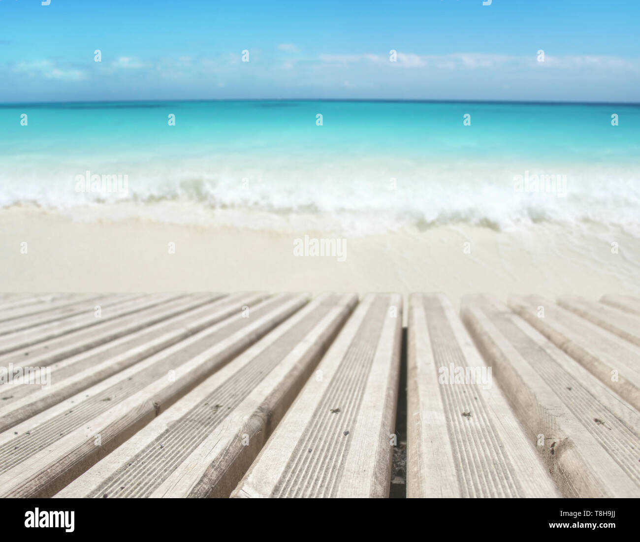 Wooden planks decking on the beach blurred background. Tropical island paradise. Sandy shore washing by the wave. Bright turquoise ocean water.  Dream Stock Photo