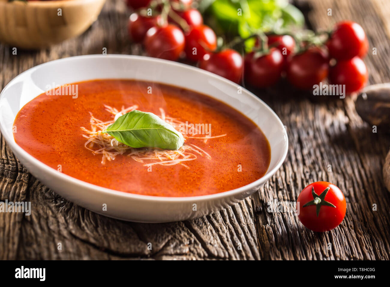 Hot tomato soup parmesan cheese and basil leave on old oal table Stock Photo
