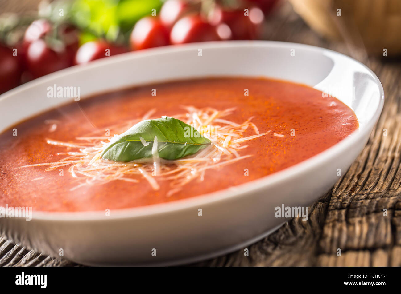 Hot tomato soup parmesan cheese and basil leave on old oal table Stock Photo