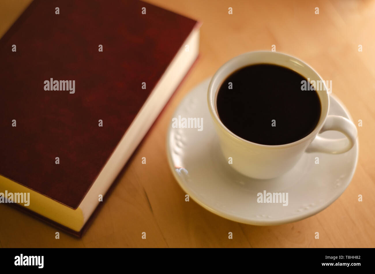 Closed book with a blank cover next to a full cup of coffee on a wooden table. Stock Photo