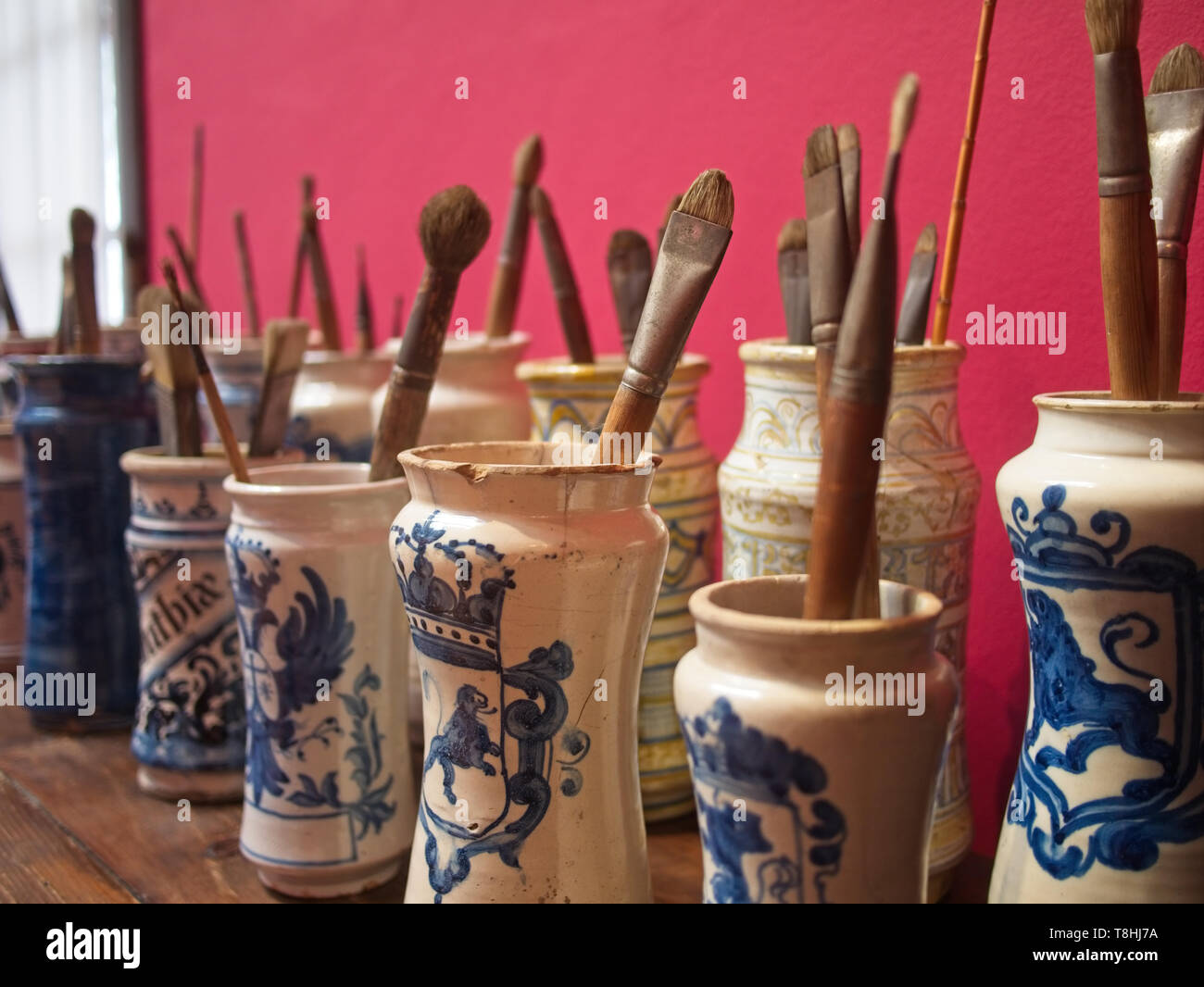 Paintbrushes in Spanish traditional porcelain vases against red wall at