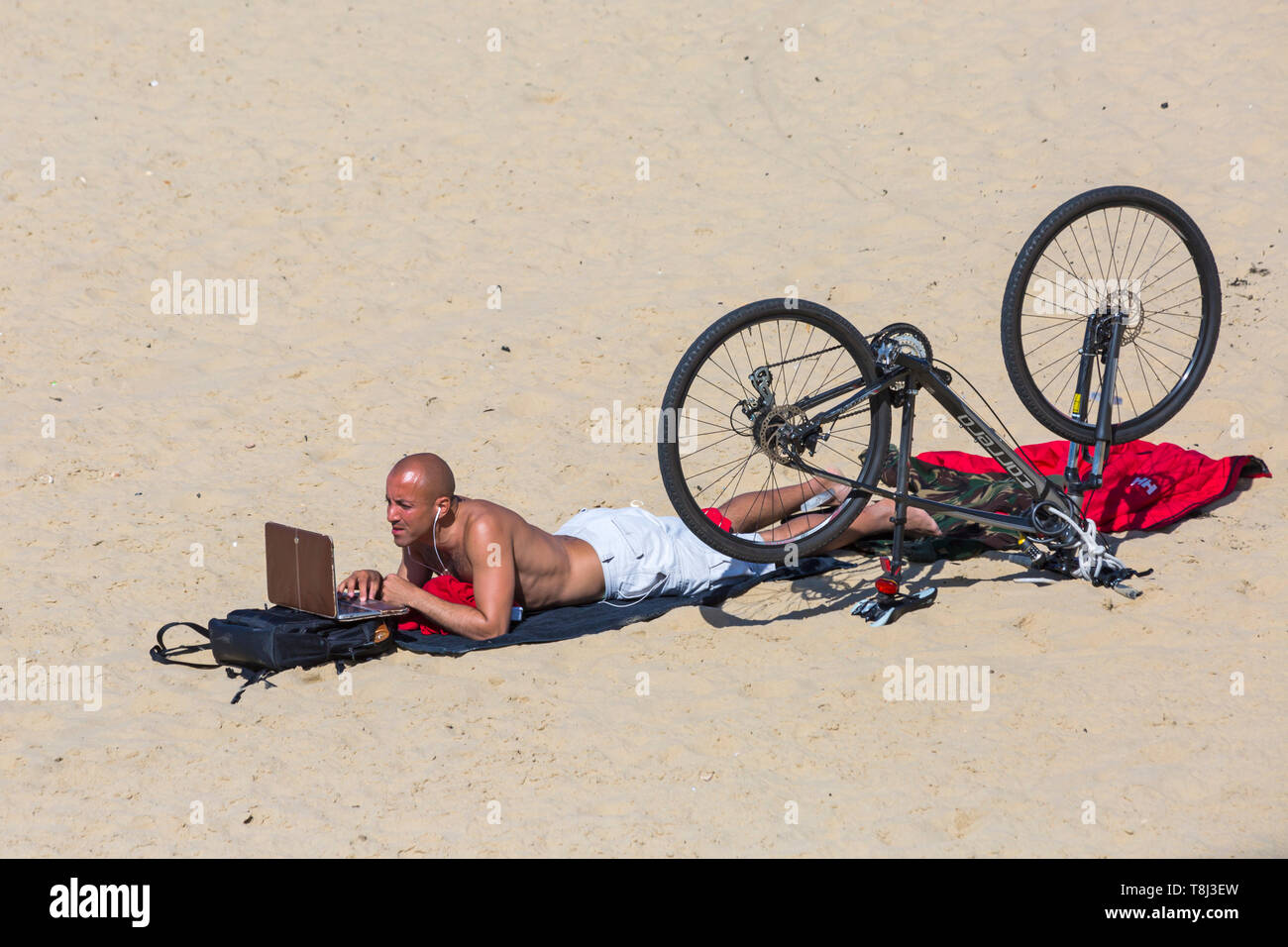 Bournemouth, Dorset, UK. 14th May 2019. UK weather: lovely sunny day, but very blowy at Bournemouth beaches, as visitors head to the seaside to make the most of the sunshine.  Man with laptop and bike on the beach.  Credit: Carolyn Jenkins/Alamy Live News Stock Photo