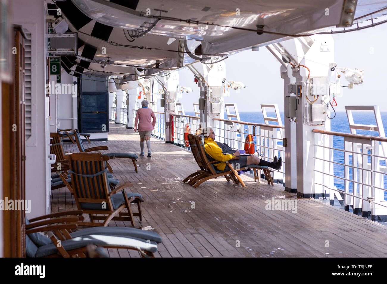 Passengers aboard a cruise ship relaxing on deck chairs and walking the ...