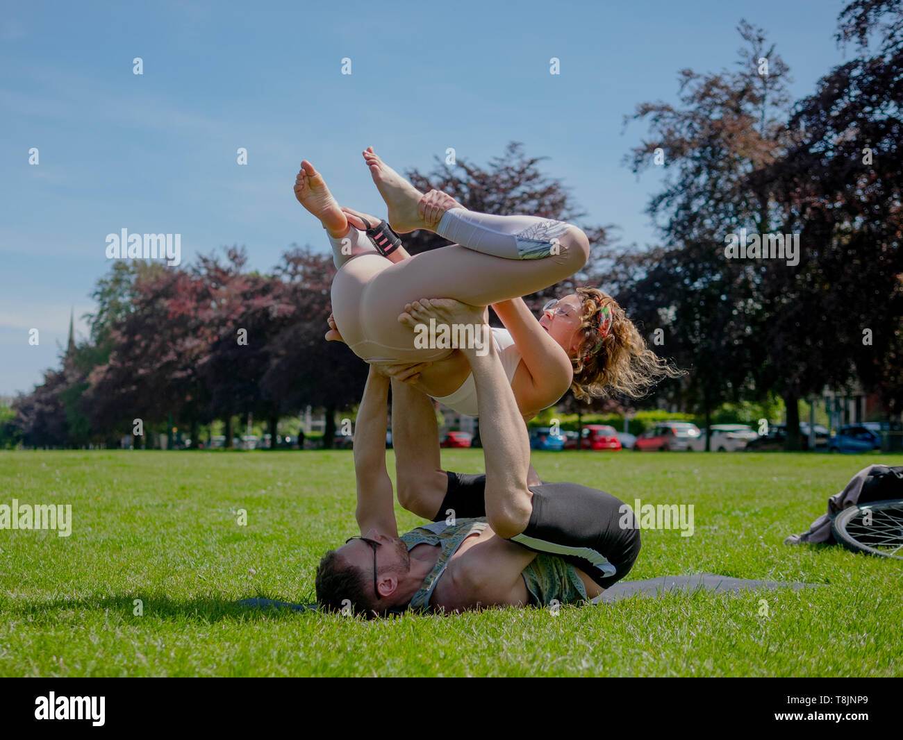 Young athletic couple in love performing acro yoga in Roath park on a bright sunny day. Stock Photo