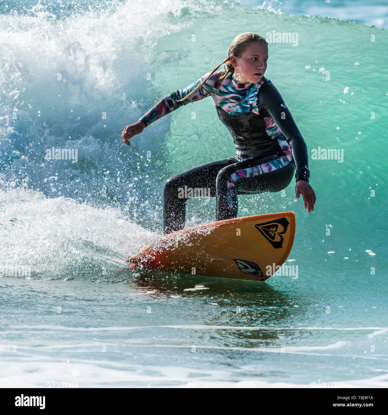 Surfing action as a young teenage female surfer rides a wave at Fistral in Newquay in Cornwall. Stock Photo