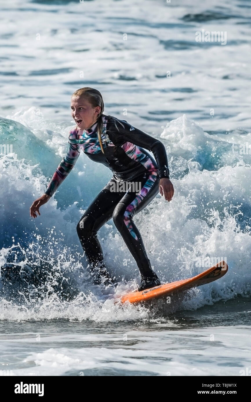 Surfing action as a young teenager female surfer rides a wave at Fistral in Newquay in Cornwall. Stock Photo