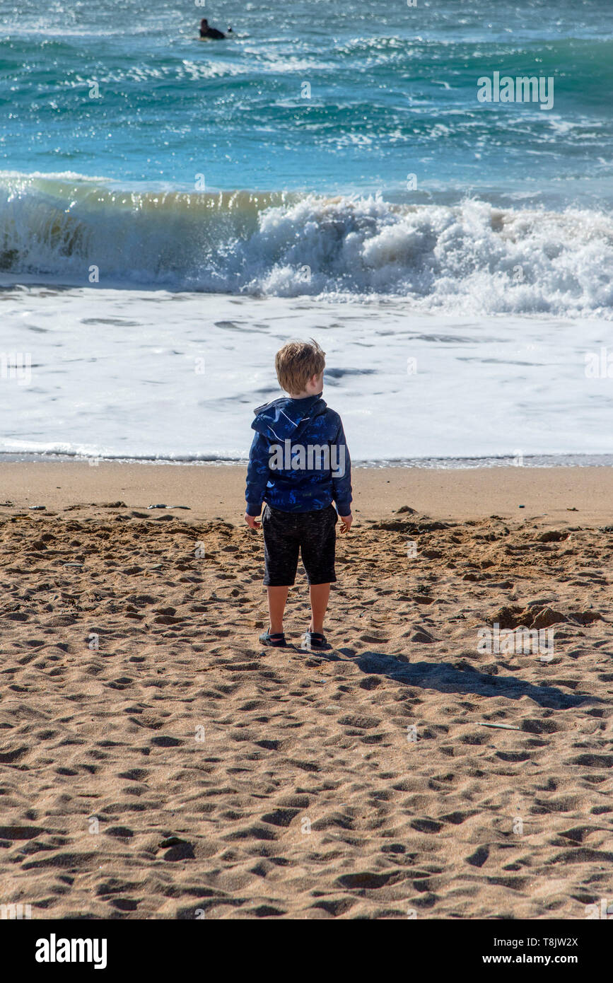 A young boy standing alone on the shoreline gazing out to sea on Fistral Beach in Newquay in Cornwall. Stock Photo