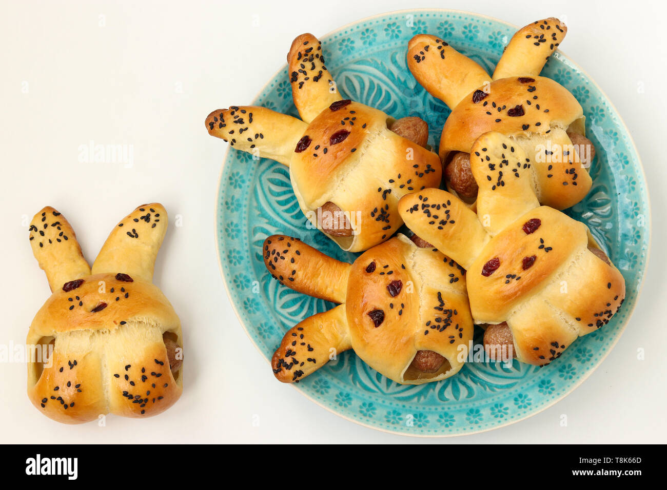 Buns in the form of hares with sausages are located on a blue plate on a white background, culinary idea for children, top view Stock Photo