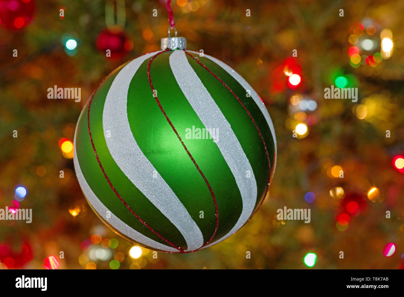 large green and white and red christmas tree ornament with defocussed tree and lights behind it Stock Photo