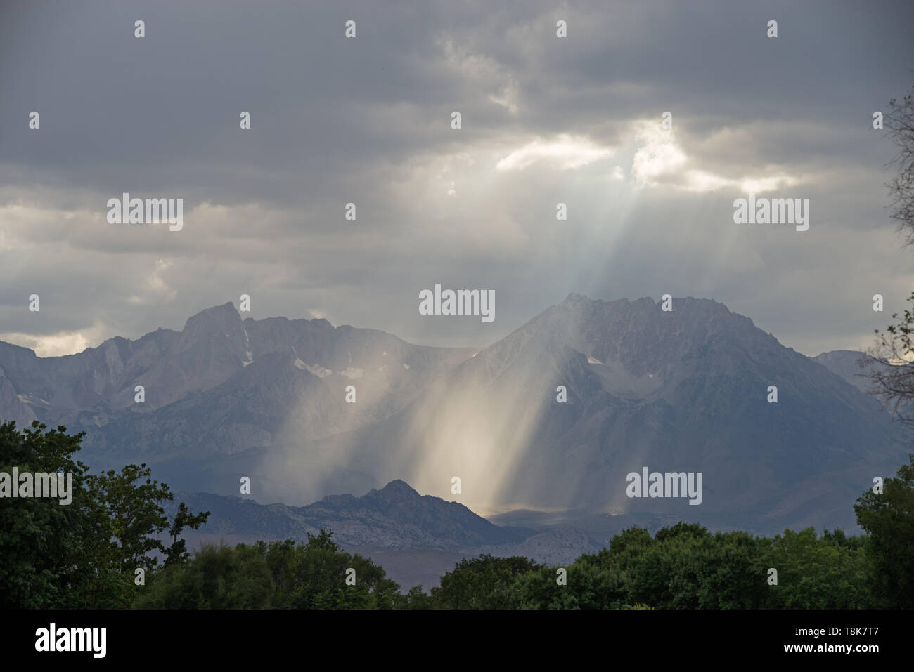 sunrays stream down from a gap in the clouds in front of the Sierra Nevada Mountains Stock Photo