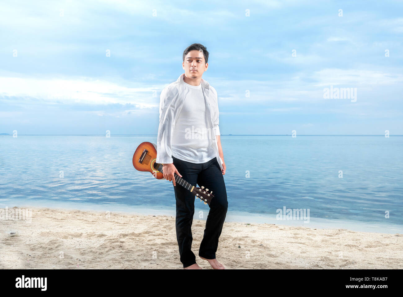 Asian businessman in white clothes holding guitar on the beach. Summer vacation Stock Photo