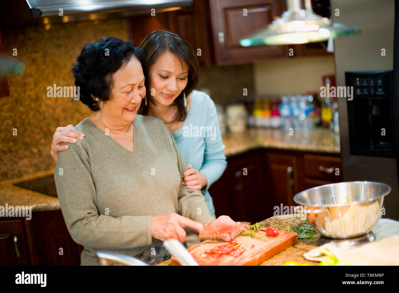 Woman hugging mother as she cuts tomatoes Stock Photo - Alamy