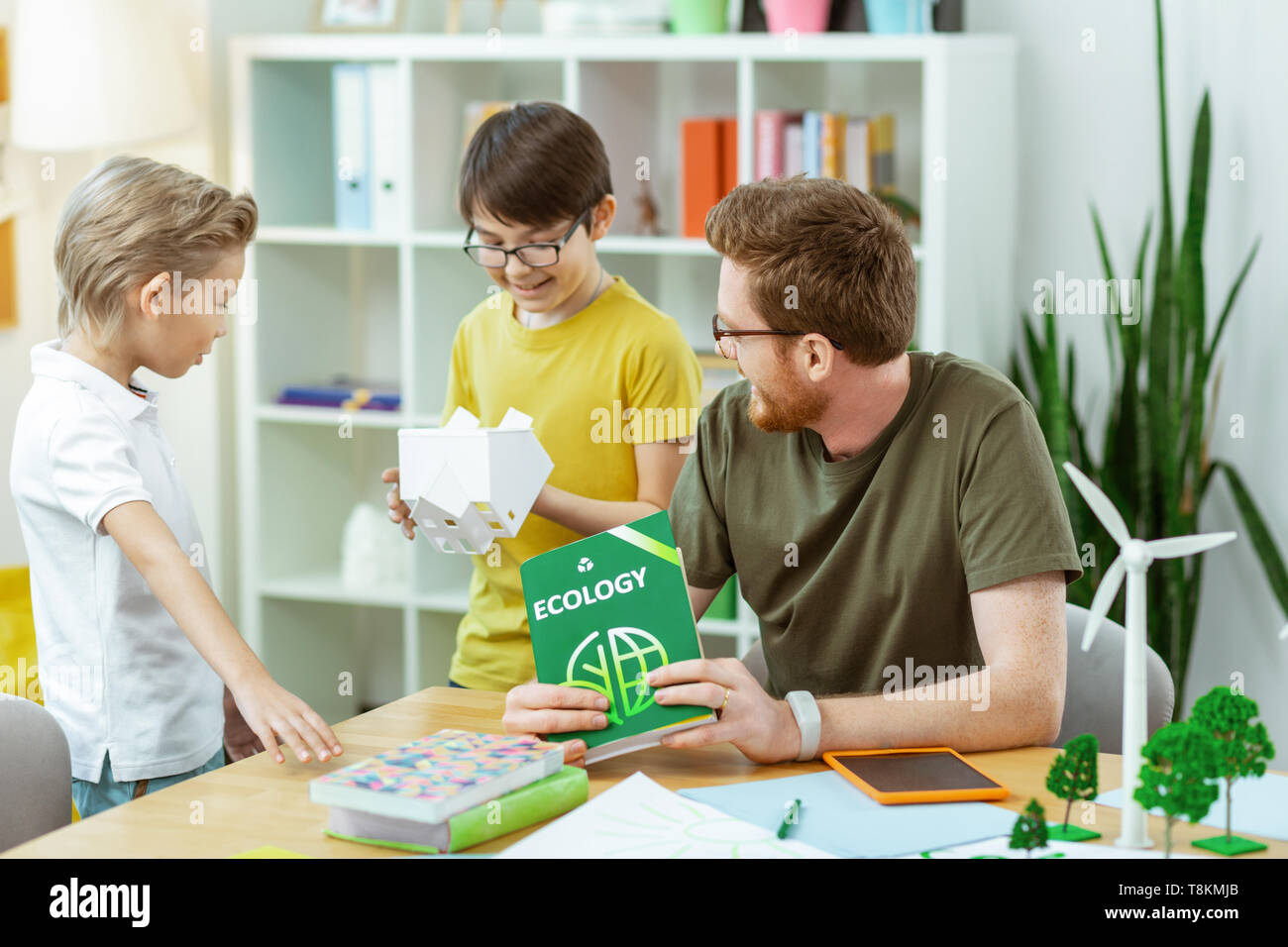 Smiling dark-haired boy inspecting plastic house during lesson Stock Photo