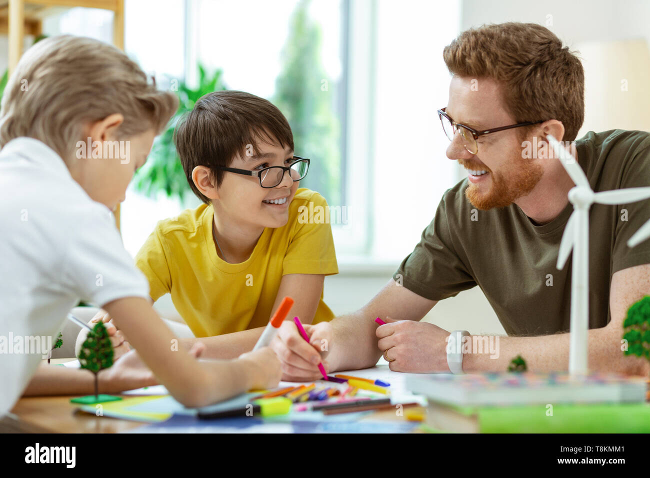 Laughing short-haired man in clear glasses helping little boys Stock Photo