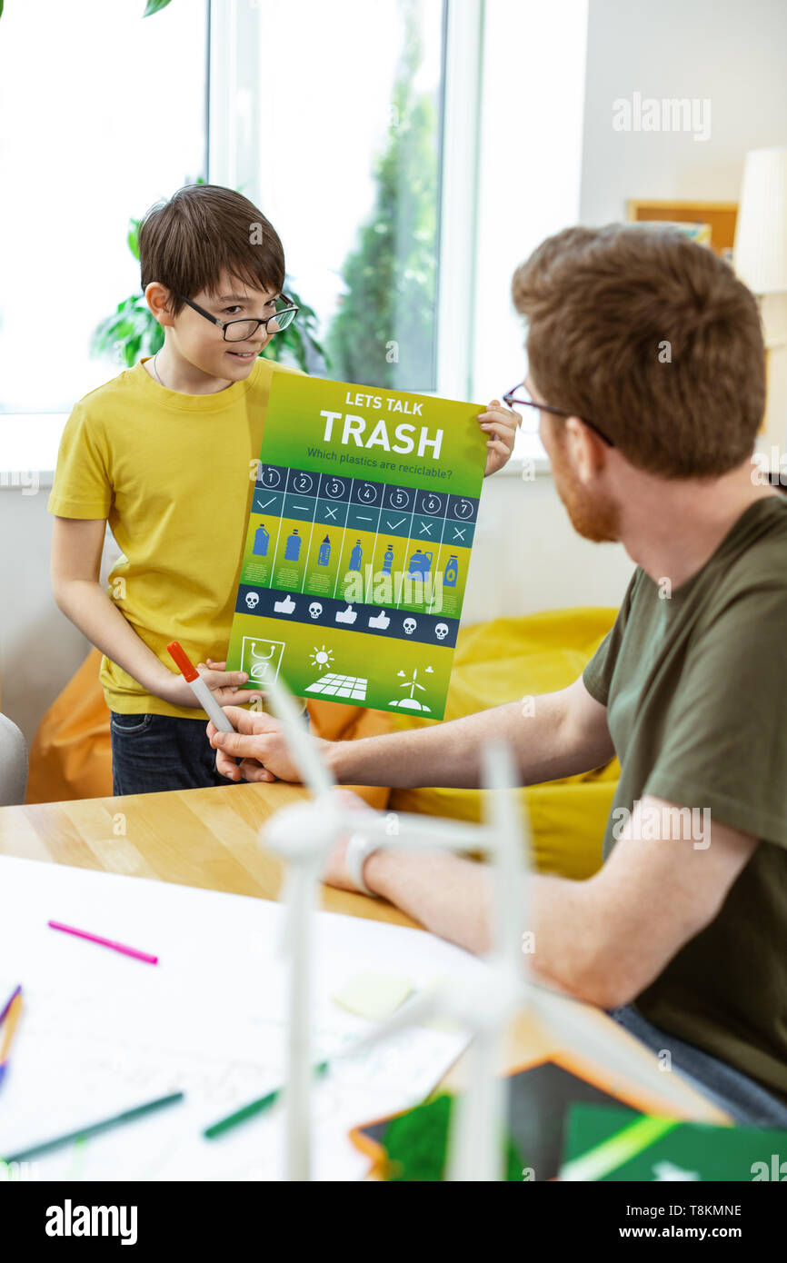 Positive dark-haired pupil carrying informative poster and explaining details Stock Photo