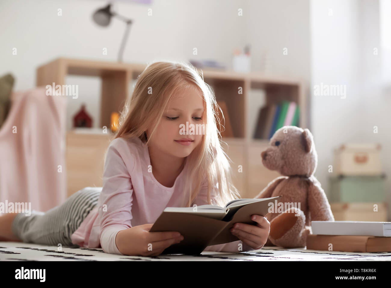 Cute little girl reading book on floor at home Stock Photo