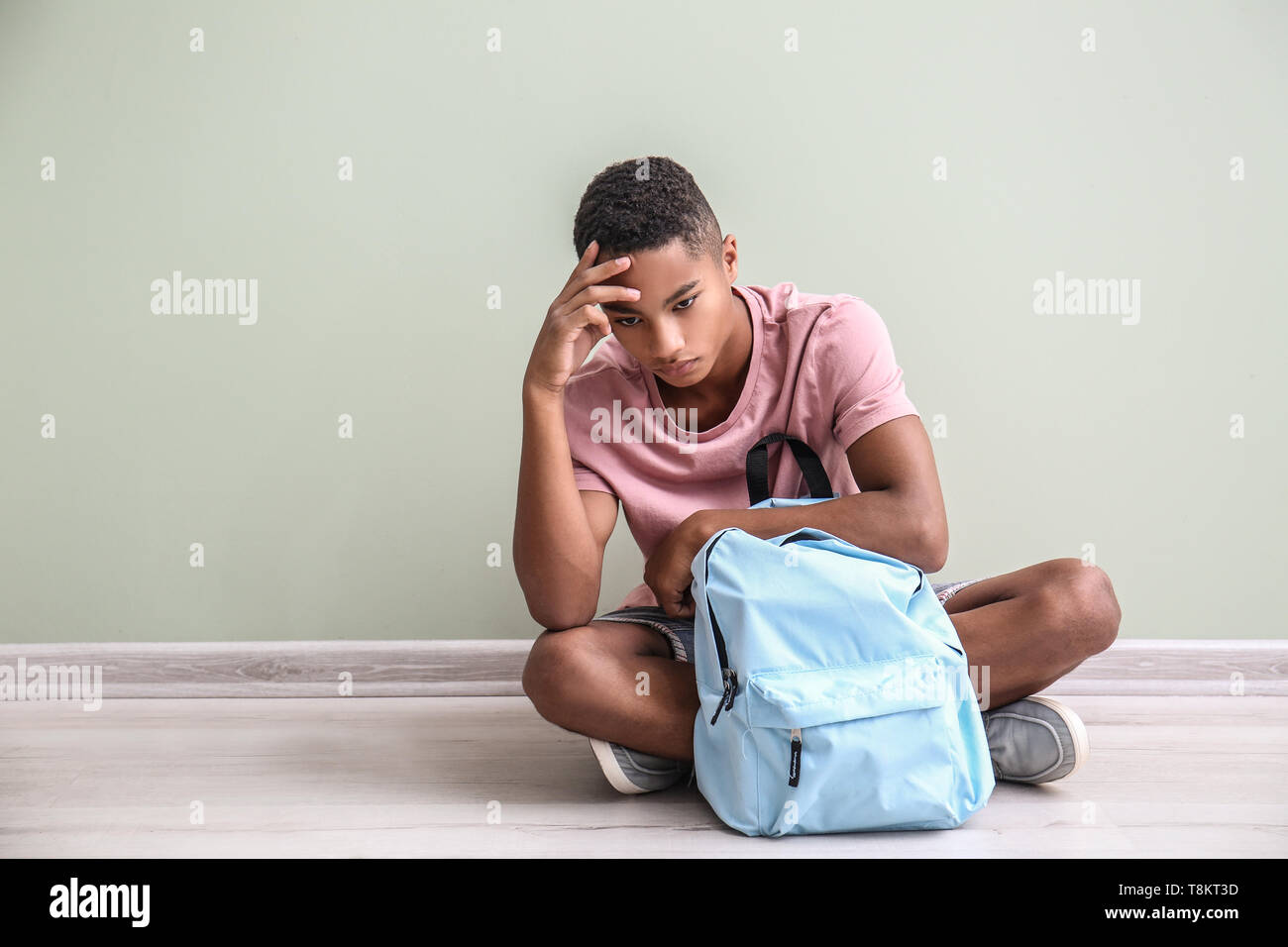 Sad African-American teenage boy sitting on floor indoors. Bullying at school Stock Photo