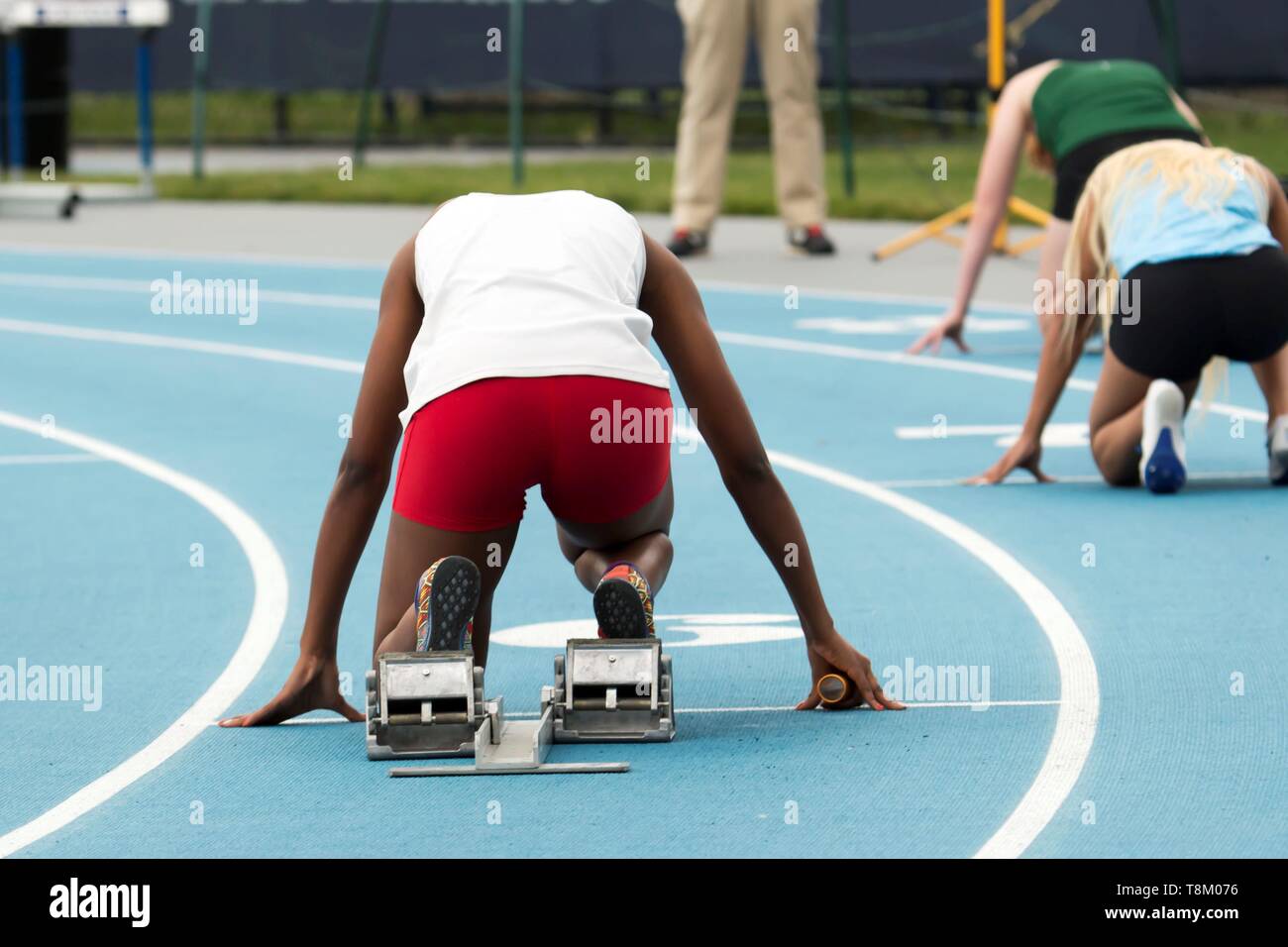 A high school female is in the starting blocks ready to start a relay race at a track and field competition Stock Photo